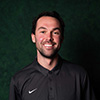 Owen Munro indoor headshot against a dark background smiling at the camera wearing a black polo with the Nike swoosh logo.