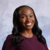 Mya Clark indoor headshot wearing a dark purple outfit against a light gray background.