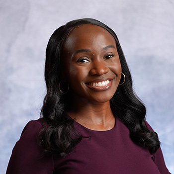Mya Clark indoor headshot wearing a dark purple outfit against a light gray background.