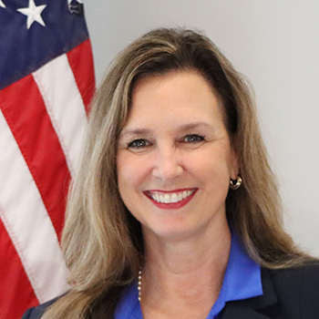 Belinda Small indoor headshot with a United States of America flag in the background.