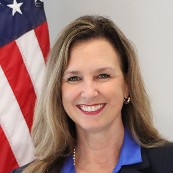 Belinda Small indoor headshot with a United States of America flag in the background.