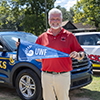 Christopher Roney outdoors holding a University of West Florida pennant while standing in front of two SUVs.