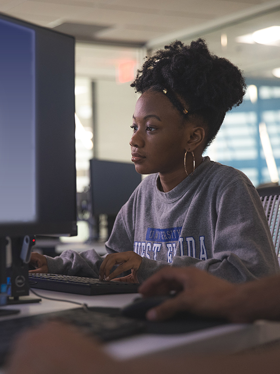 Cybersecurity student looking at a monitor in a computer lab.