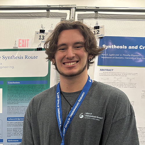 Ethan Sanz smiling at the camera while standing in front of a research poster board.