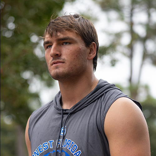 Jake Robinette outdoors in front of trees while wearing a West Florida Football sleeveless hoodie.