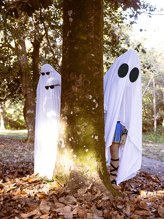 Two students and UWF mascot Argie the Argonaut dressed like ghosts for Halloween peeking around a tree.