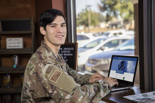 Man in military uniform in a coffee shop accessing UWF online classes on a laptop.