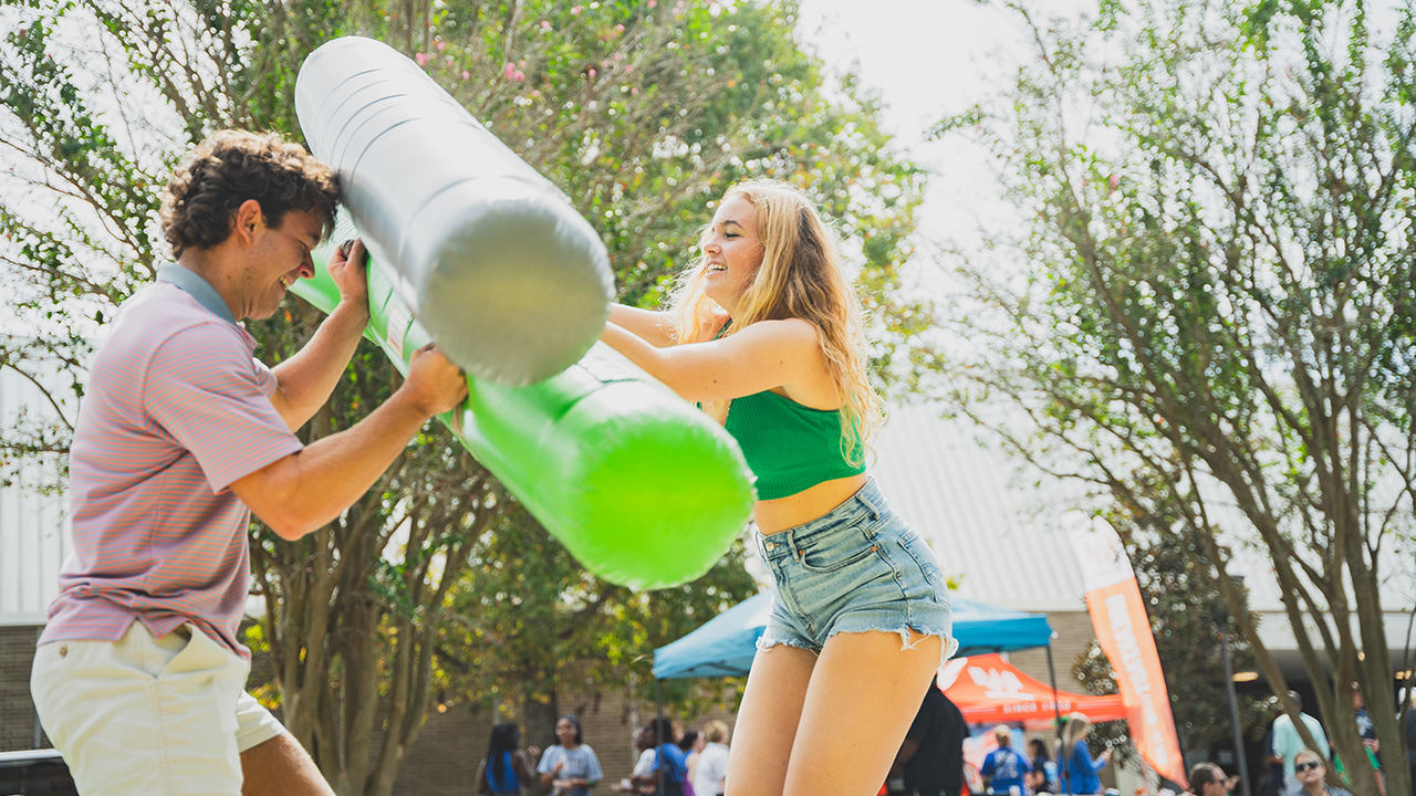 Two people jousting with inflatable equipment