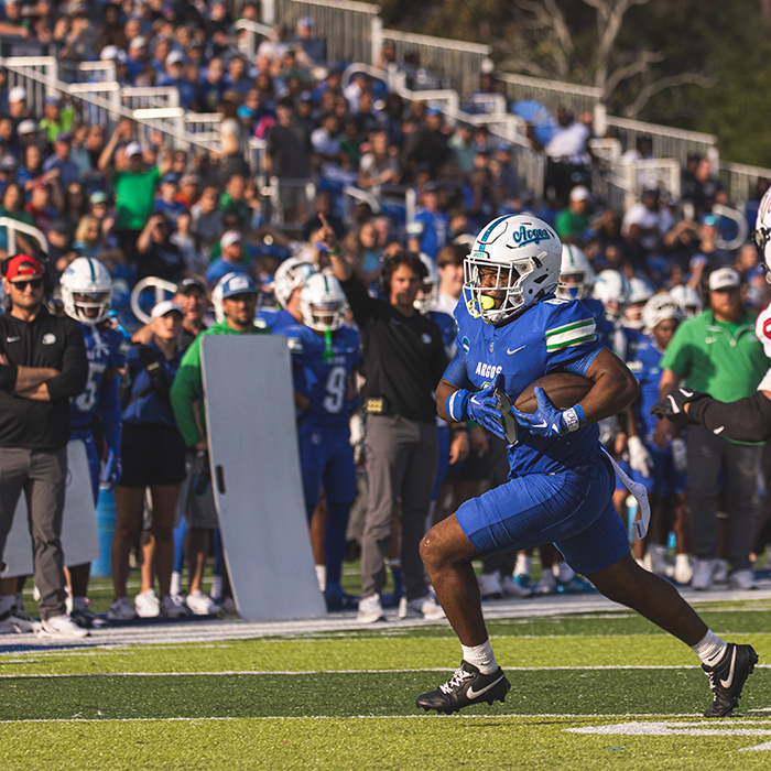 Argo player running with the ball in the foreground. Stand full of fans in the background