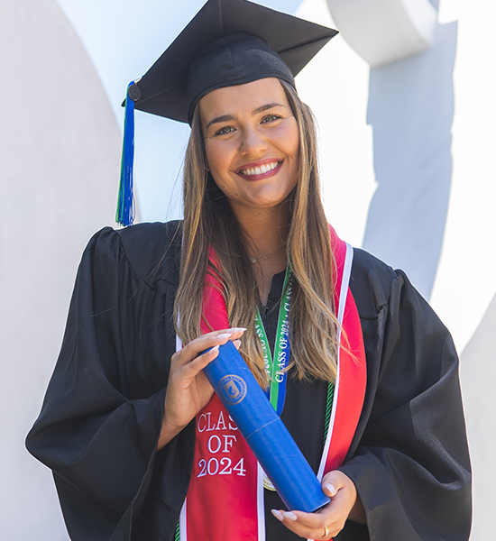 A UWF graduate smiling in cap and gown attire while holding a diploma tube.