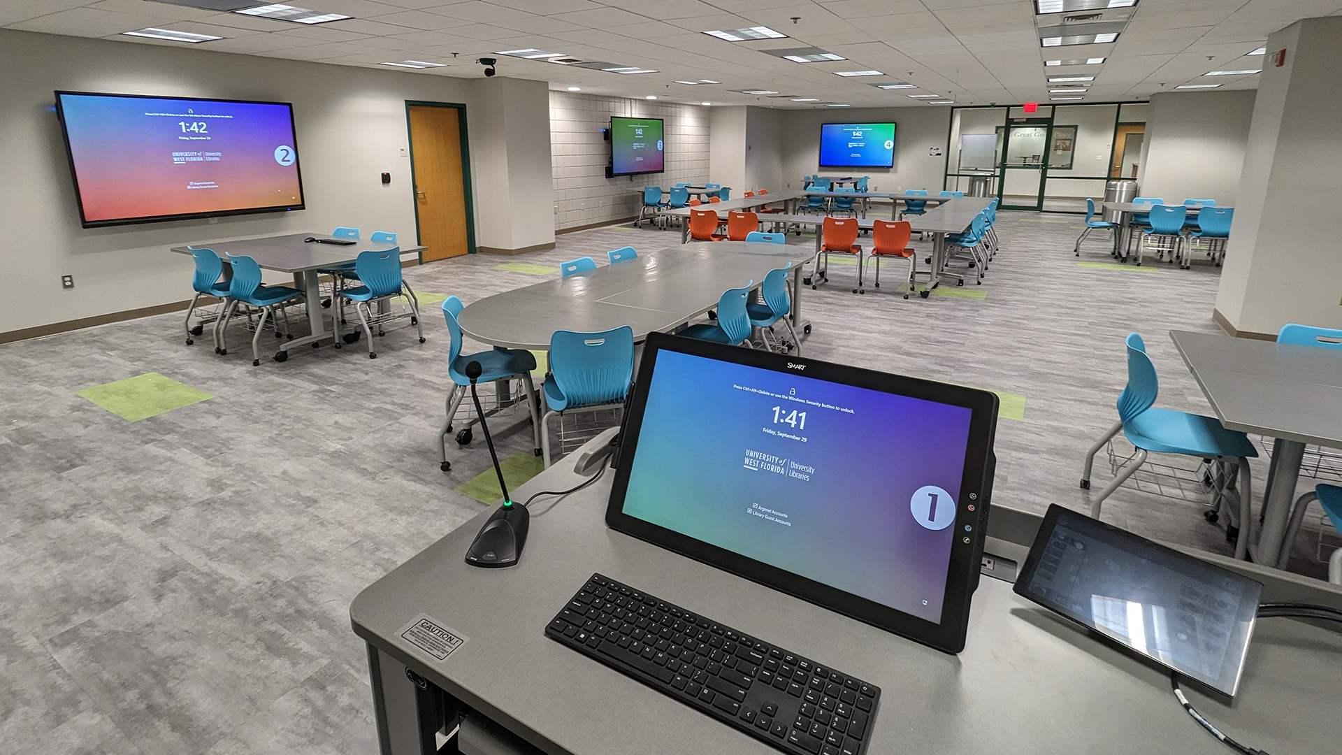 Modern library workspace with colorful chairs, wall displays, and AV control station.