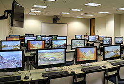 Computer lab with images on monitors, whiteboard, and wall-mounted TV screen.