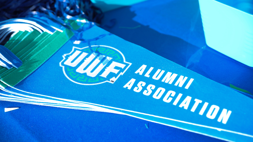 A blue pennant with the UWF Alumni Association shield logo and the words Alumni Association rests on a blue tablecloth