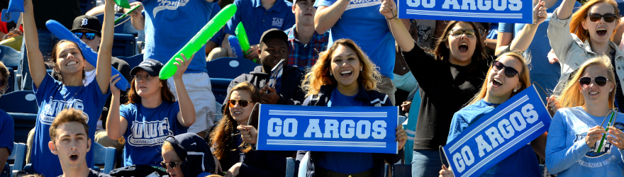 fans in the stands at a uwf football game cheer and hold Go Argos banners
