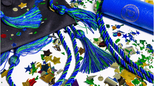 Blue and green graduation cords, tassels, a black graduation cap, and a blue diploma cover surrounded by colorful confetti.
