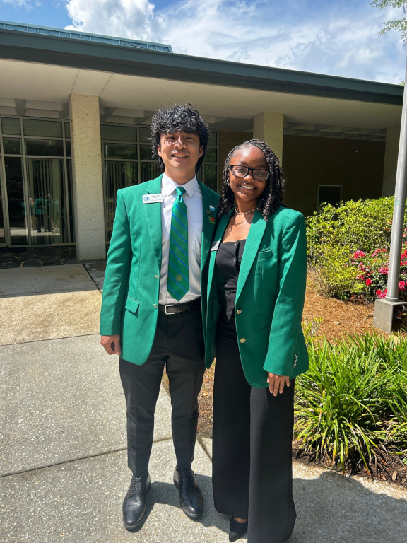 Two Student Ambassadors stand together wearing their green jackets.