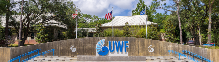 The American flag, Florida flag and UWF flag fly high above the new UWF signage at the entrance to campus.