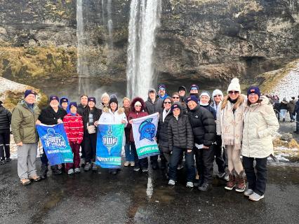 Travelers pose for a group photo in front of a rocky cliff with a waterfall.