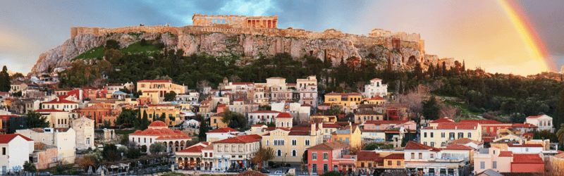 The Acropolis and Parthenon overlooking Athens buildings under a dramatic sky with a bright rainbow.