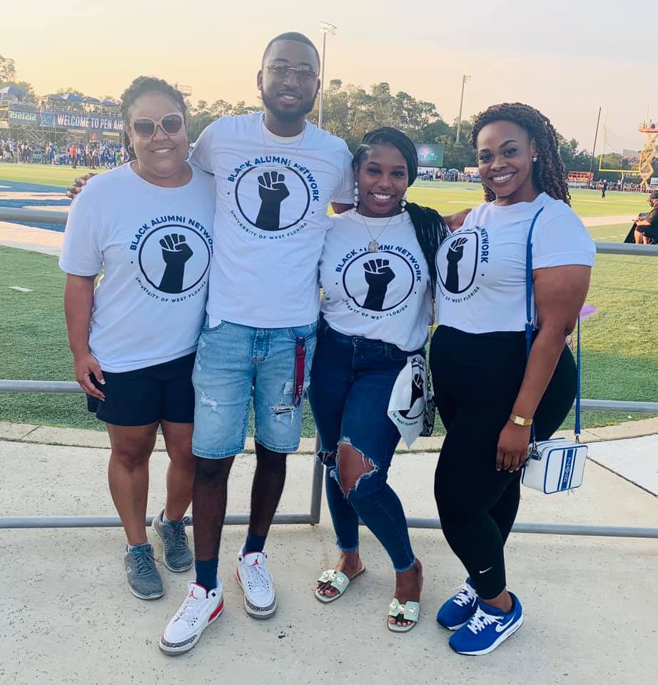 Four members of the black alumni network pose together at a football game in matching tshirts