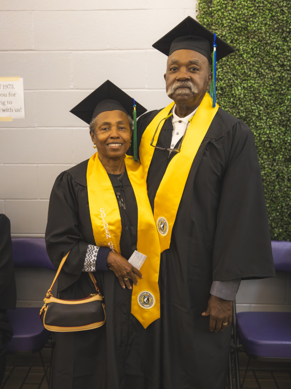 A pair of UWF Golden Graduates pose in their cap and gown with the golden stole.