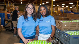 Two alumnae stand with canned items at Manna Food Bank during the 2025 Founders Week Argos Day of Service.