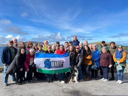 A group of alumni and guests pose in Ireland on the bluffs with a UWF Flag