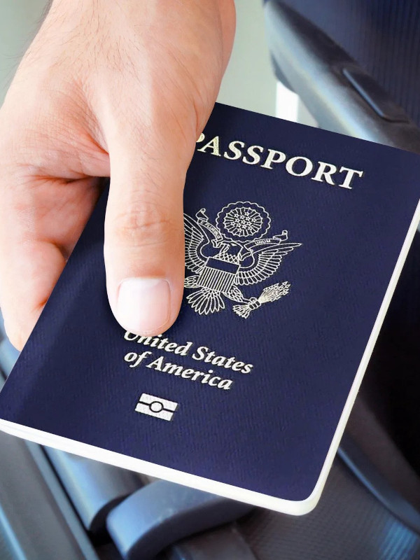 A hand holds a US Passport on top of a suitcase.