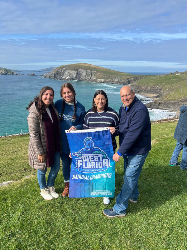 A group of alumni pose with a UWF banner on a cliffs edge in Ireland.