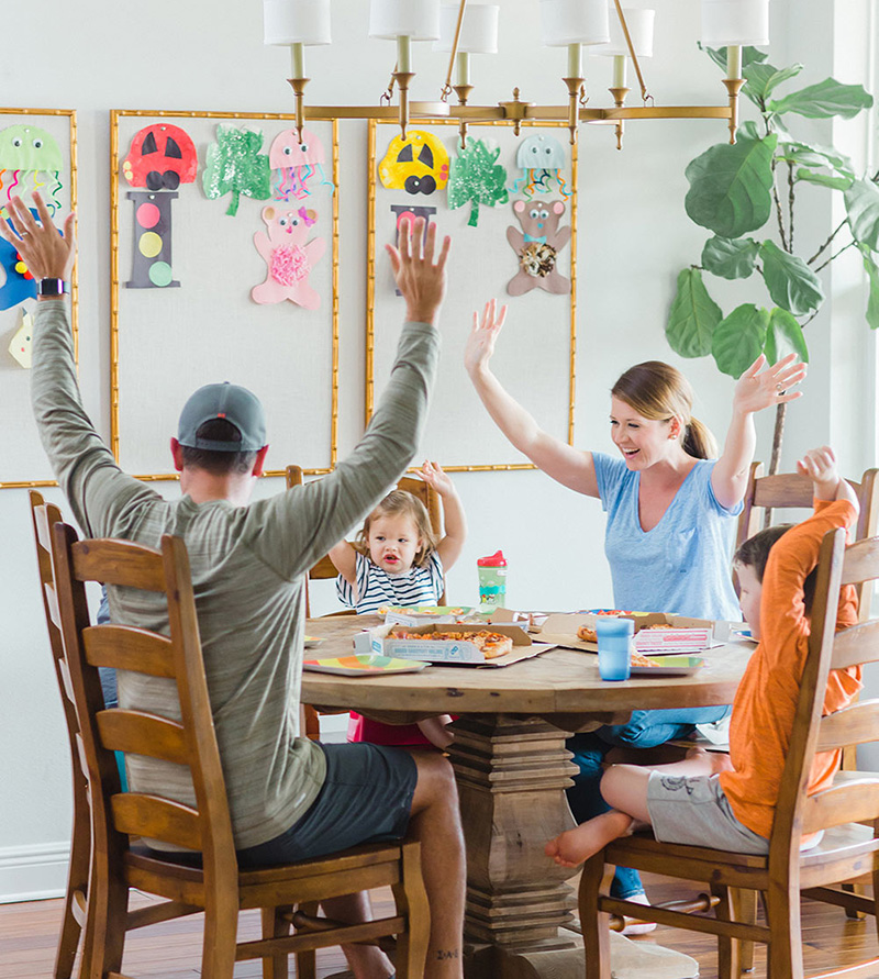 Emily Ley playing at the dinner table with her family, arms raised