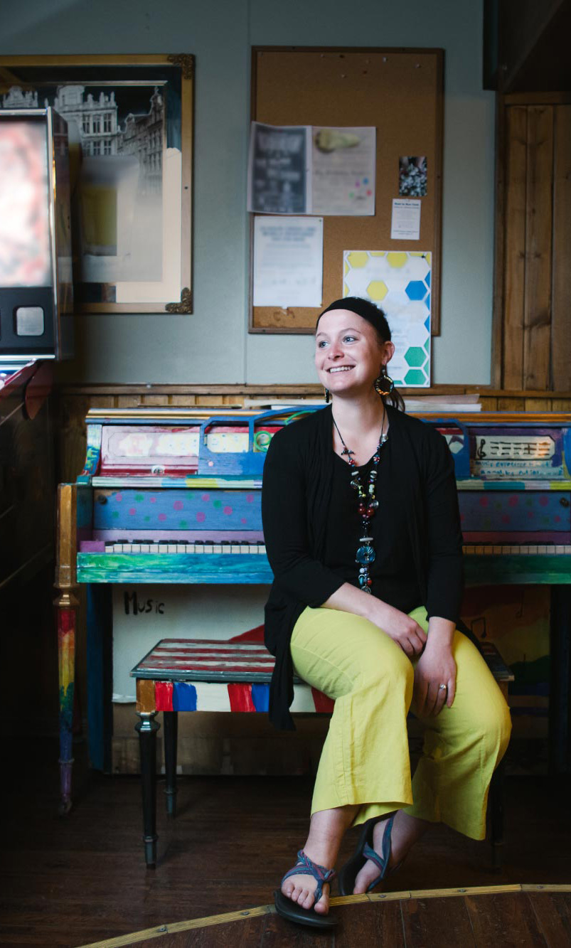 Dr. Patricia Izbicki sits smiling at a colorfully painted piano