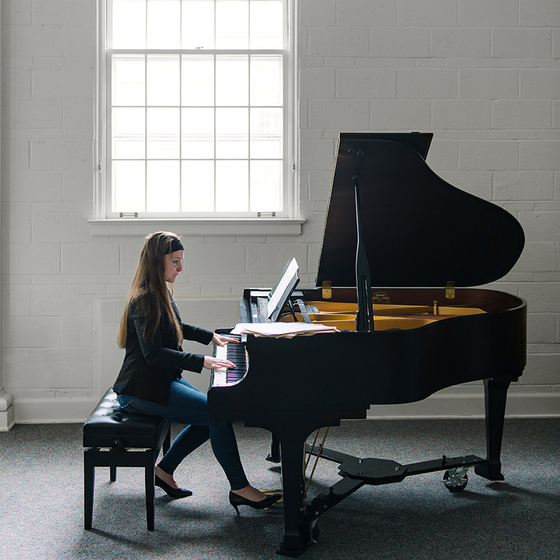 Dr. Patricia Izbicki playing a grand piano in front of tall bright windows