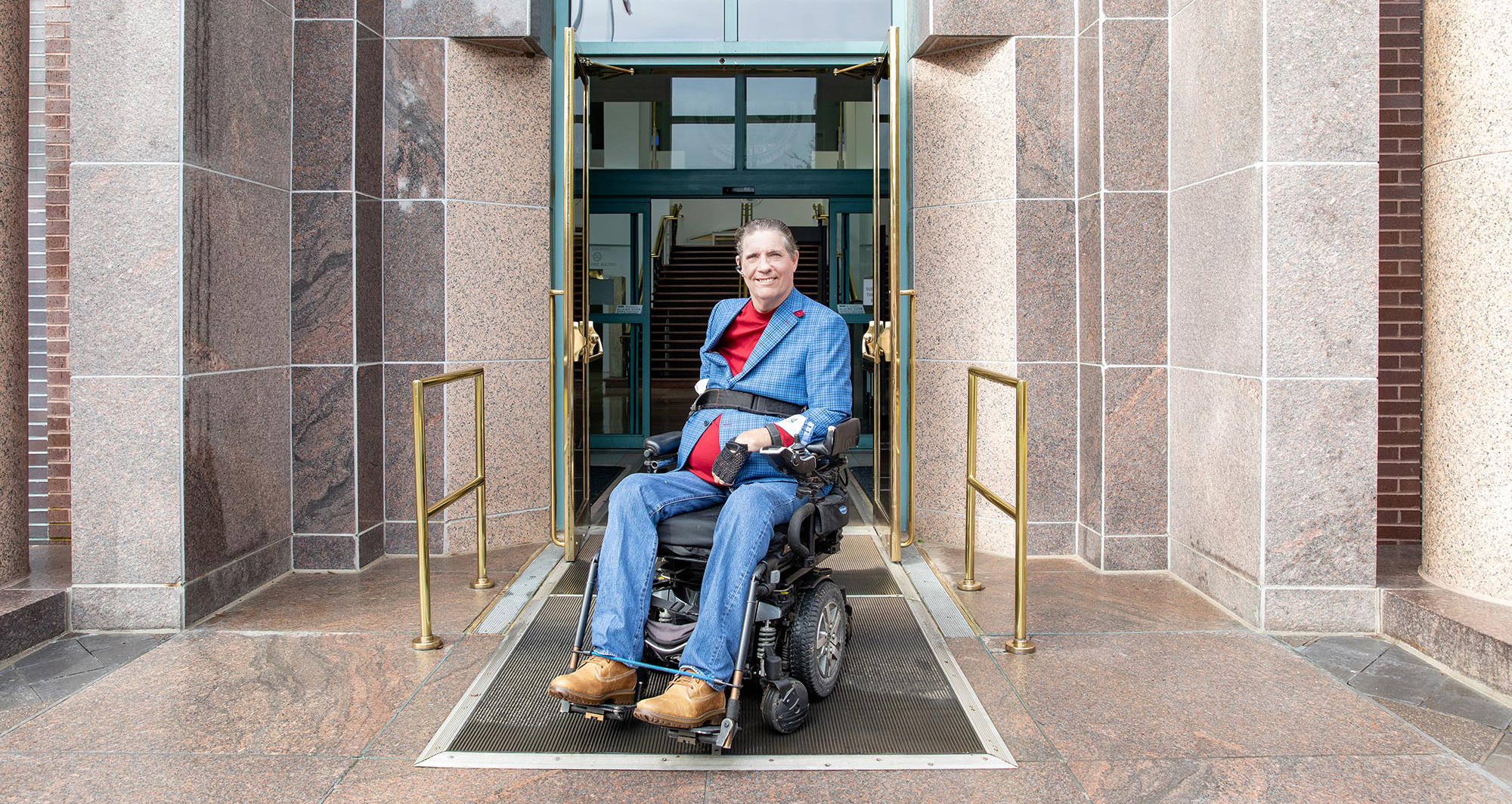 JR Harding in a wheelchair at the accessible entrance to a public building