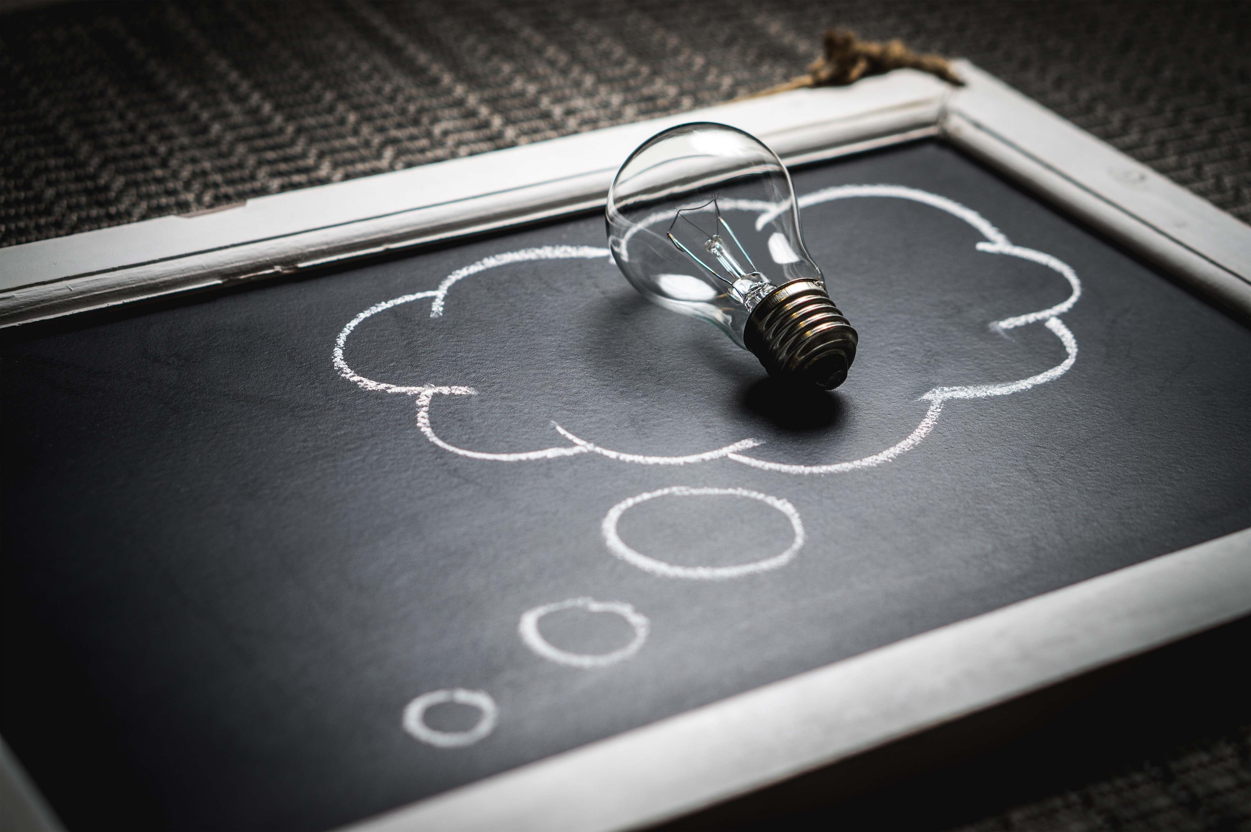 Chalkboard drawing of an idea cloud that has a light bulb laying on the board inside the idea cloud.