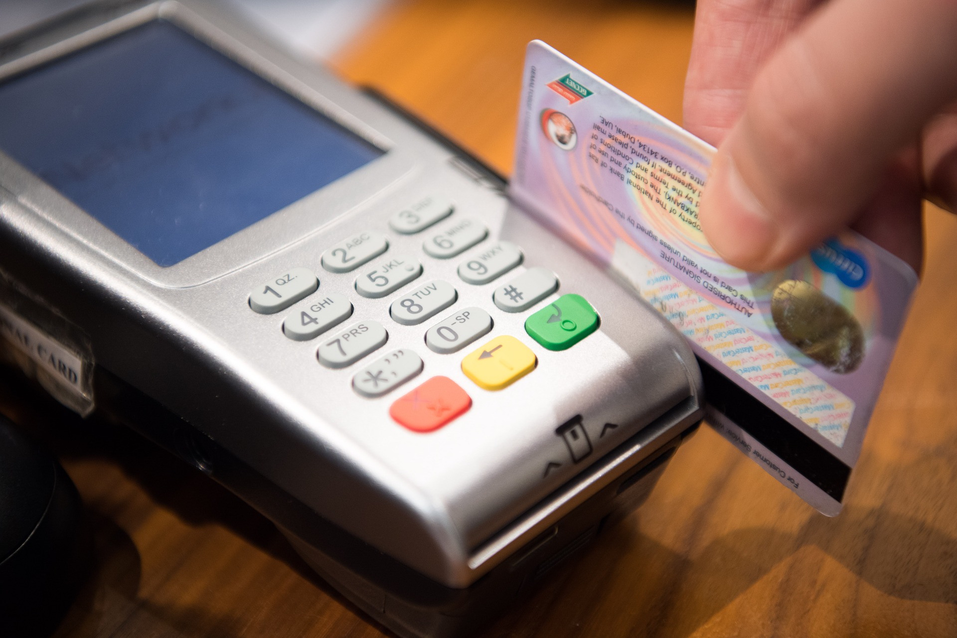 A hand swiping a credit card through a credit card reader.
