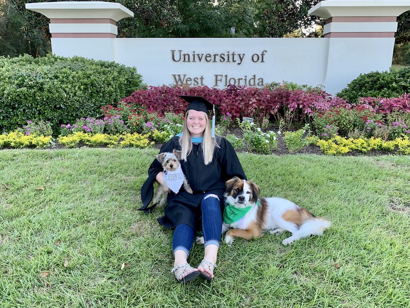 Alumni in front of UWF sign with her two dogs