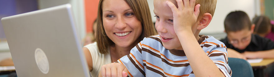 Teacher in classroom working with a student on a laptop