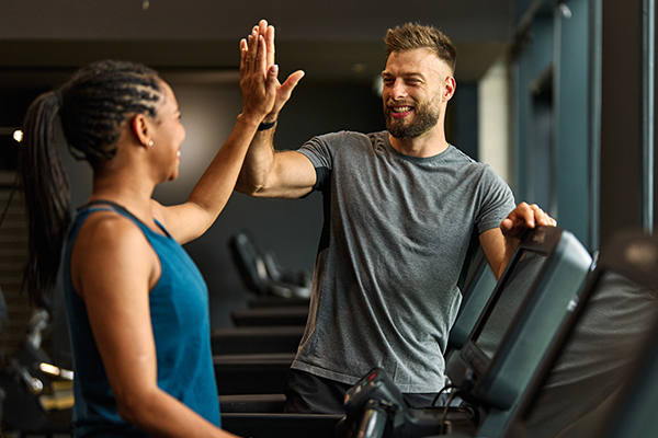 Physical trainer giving client a high five in a gym on the treadmill