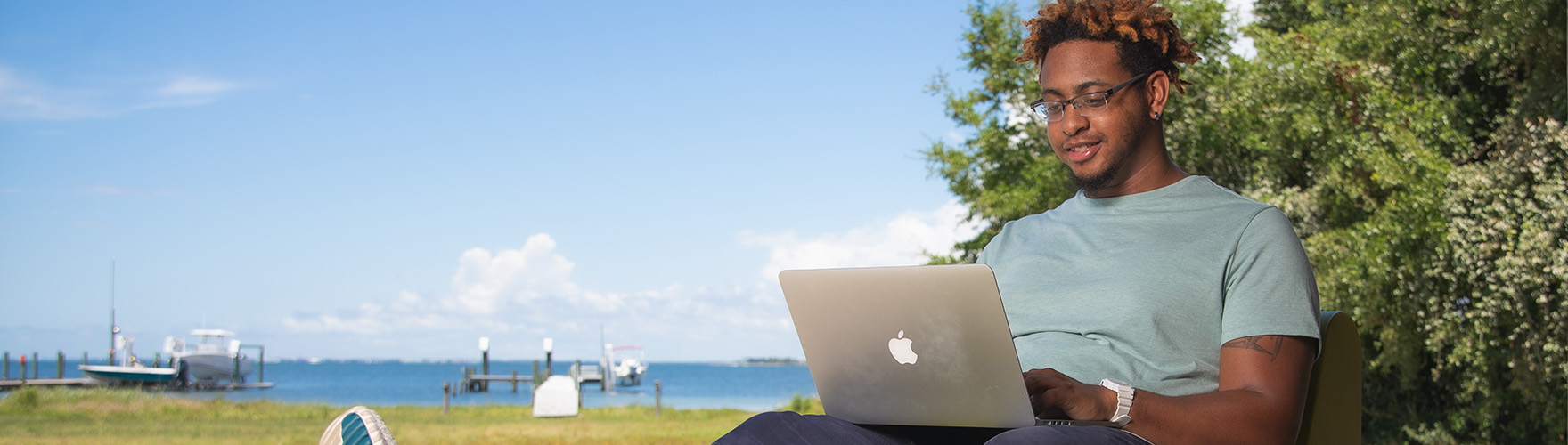 A student uses a laptop in a backyard by the water.