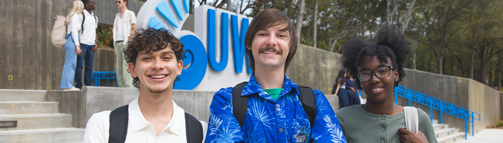 UWF students smile in front of the main campus entrance.