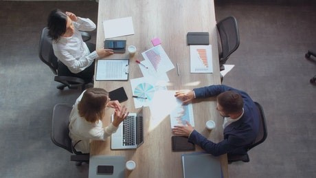 Three people meeting at a table using laptops and sharing notes.