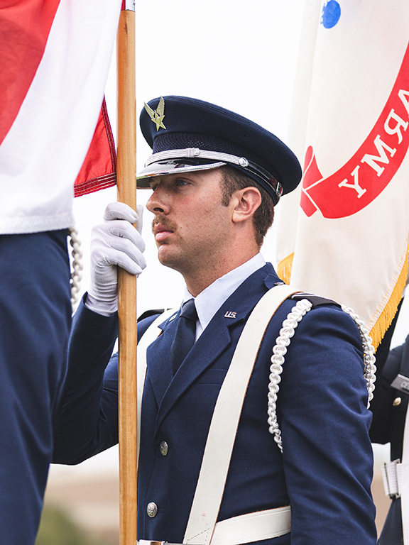 A military student in uniform carrying a pole with a flag.