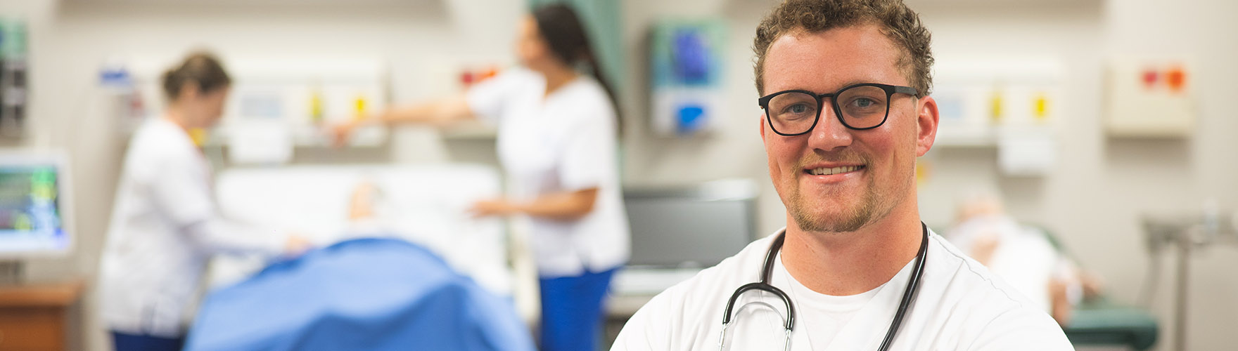 A UWF nursing student smiles while others practice in the background.