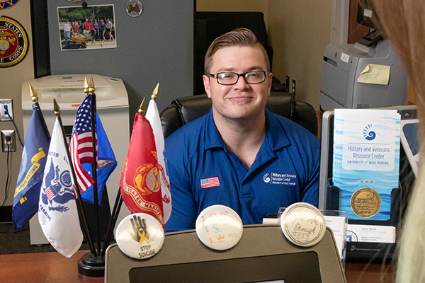 Military student sitting at an office desk with mini military flags, military theme buttons, and military program brochures displayed on the desk.