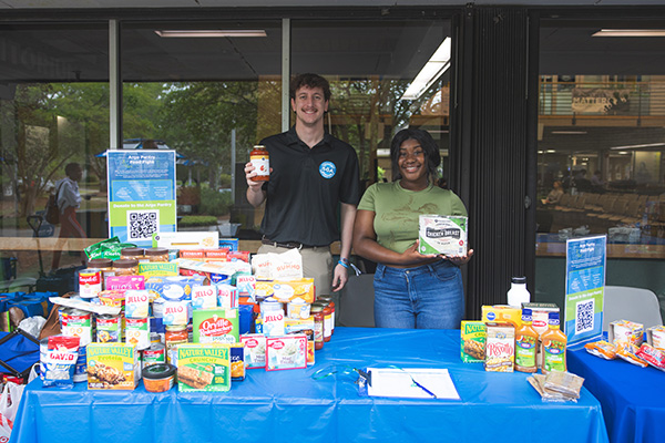 Two students behind a table displaying various cans and boxes of food.