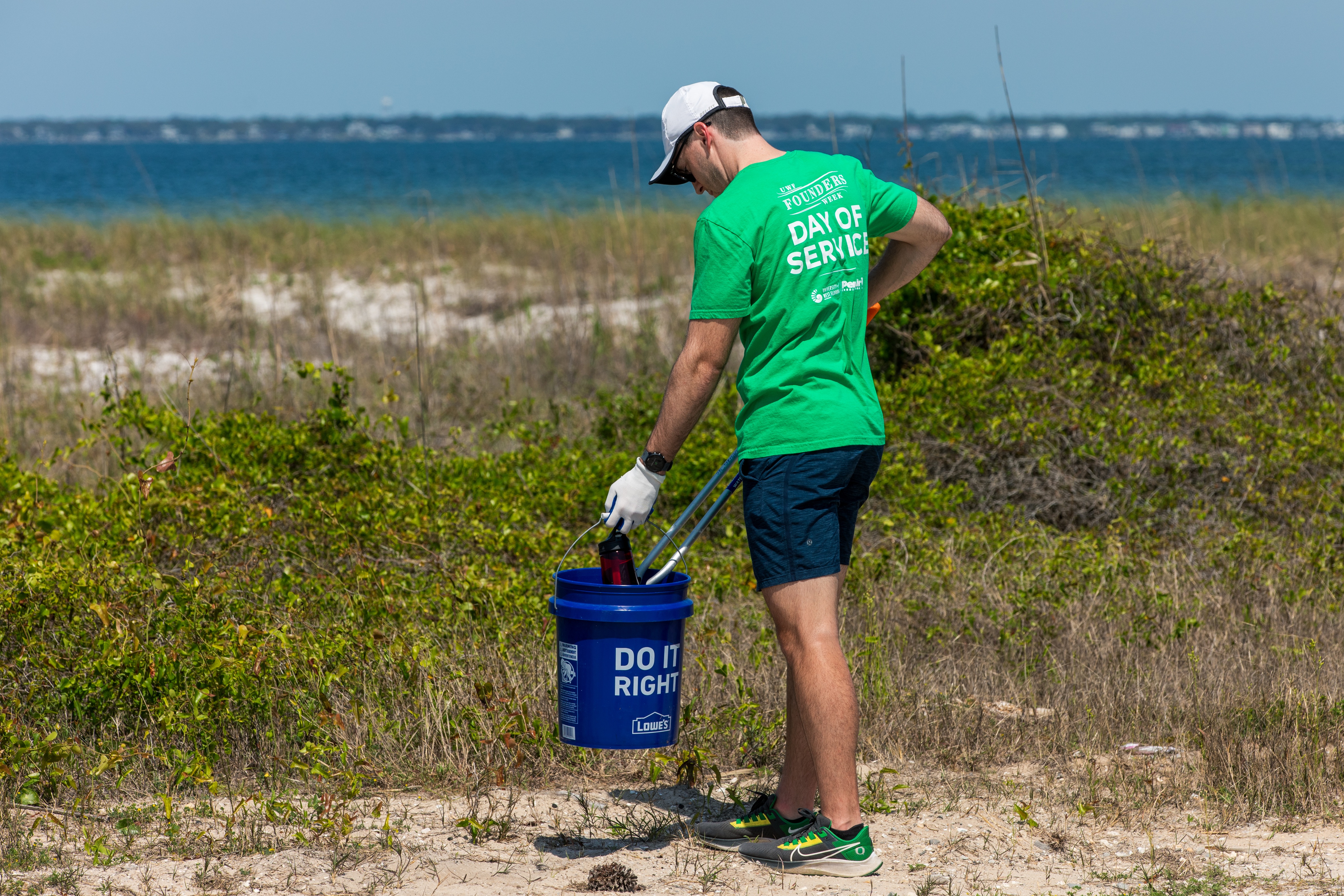 A person at a beach holding a bucket and a trash picker.