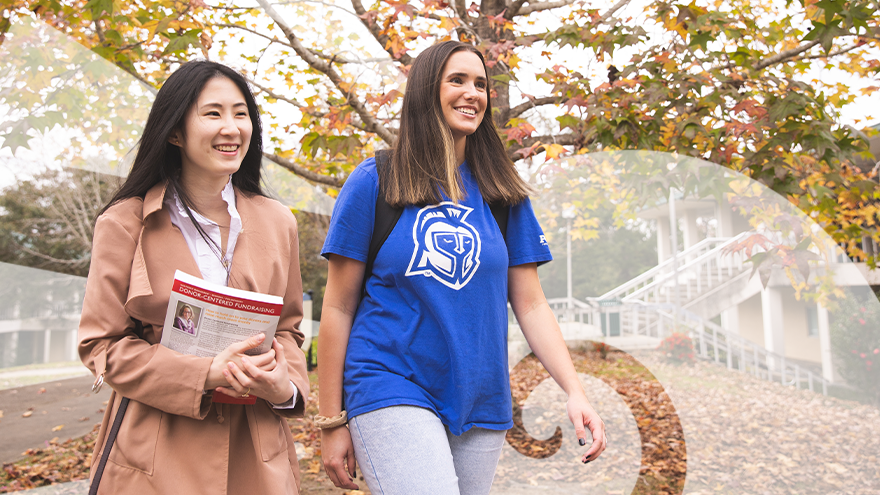 Two students walking to class by a fall seasonal tree.