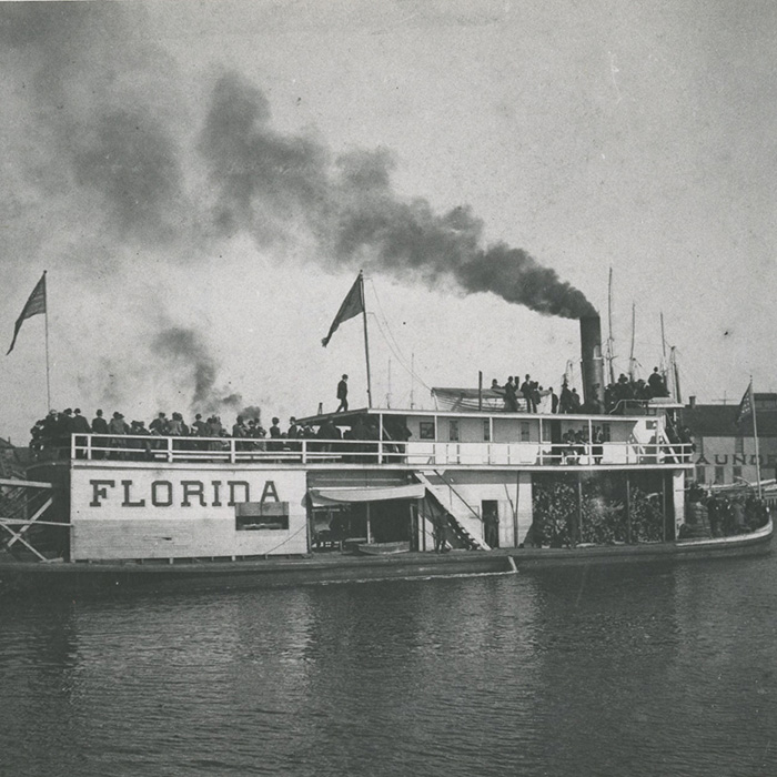 Historical steamboat on the water blowing steam with a crew onboard.