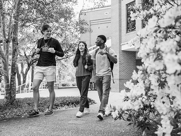 Three students walking in front of John C. Pace Library on the UWF Pensacola campus.