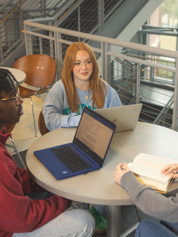 Three students with laptop computers sit at a table